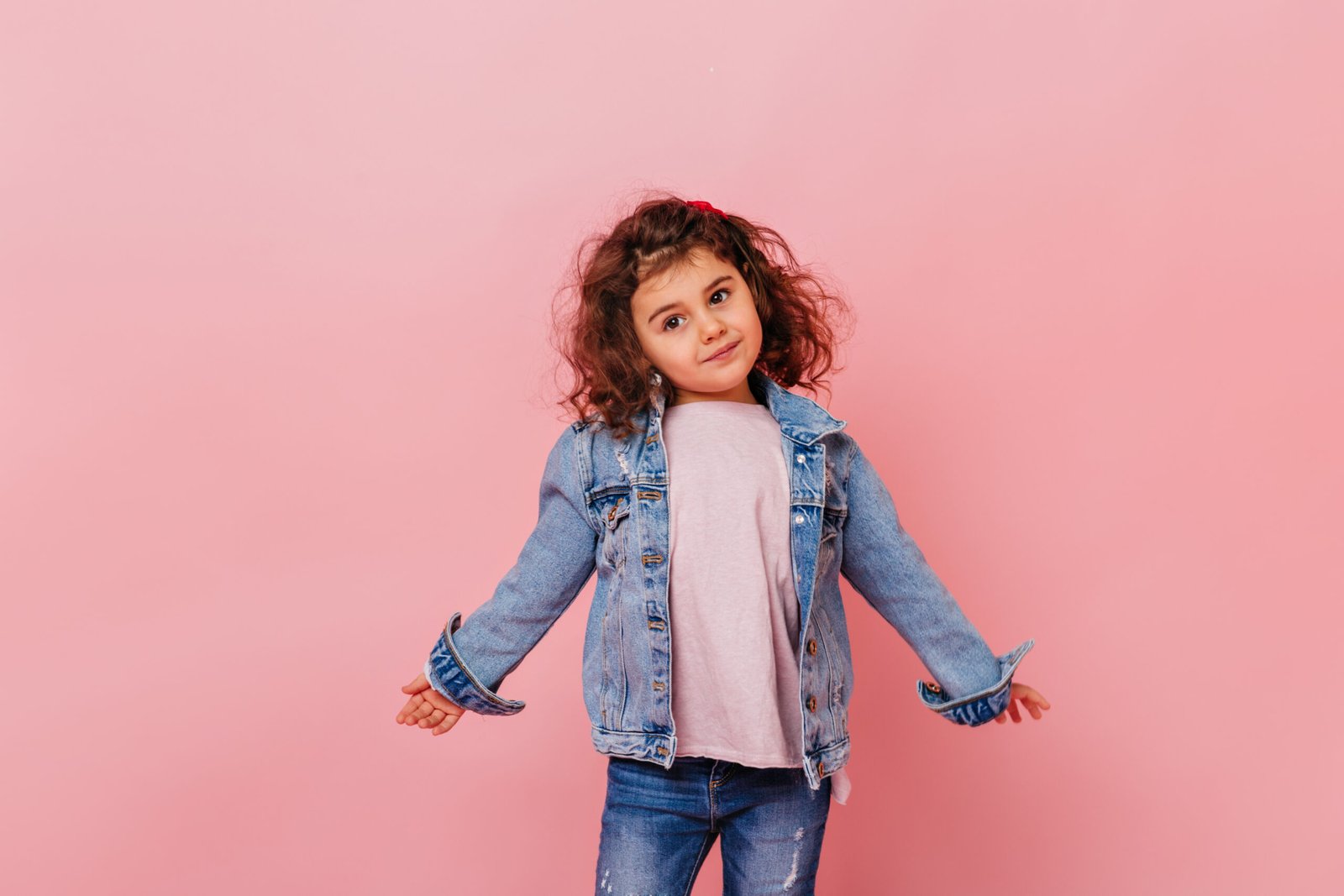 funny little girl in denim jacket looking away. studio shot of charming preteen child isolated on pink background
